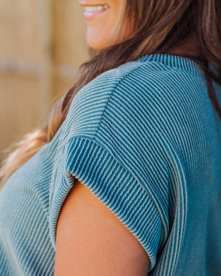 Close-up of a woman smiling in a short-sleeve blue ribbed knit top with cuffed sleeves, showcasing soft textured fabric and casual chic style.