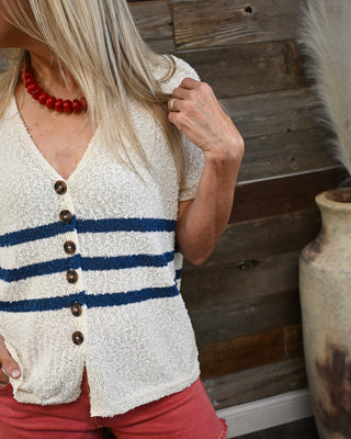 Women's cream textured knit sweater top with navy blue stripes, button-front detail, and short sleeves, styled with coral shorts for a classic coastal-inspired boutique summer outfit.