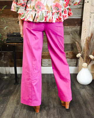 Women's hot pink high-rise wide leg pants featuring front seam detailing and a bold statement color, styled with a colorful floral ruffle top.