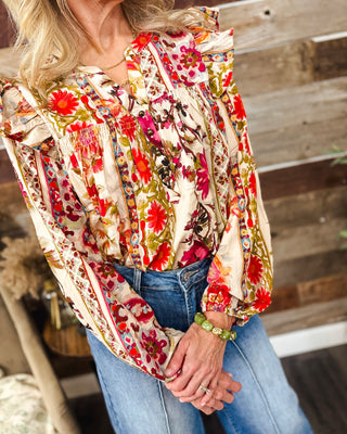 Close-up of women’s cream floral blouse with vibrant red, pink and orange flowers, ruffle shoulders, smocked yoke, button details and long balloon sleeves.