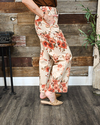 Women’s cream floral print wide-leg pants with a high-rise fit, styled with a brown top and neutral studded mules for a chic fall boutique outfit.