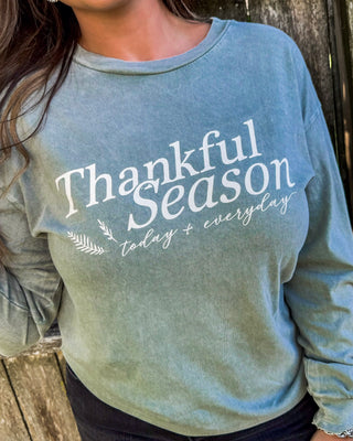 Woman wearing a faded sage green long sleeve sweatshirt with the phrase “Thankful Season today + everyday” in white script, perfect for cozy fall outfits.
