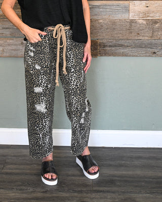 Women’s leopard print distressed jogger pants with rope drawstring waist and cropped fit, styled with black platform sandals for a casual boutique look