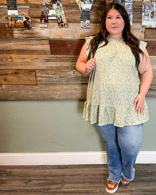Curvy women’s green floral top with flutter sleeves and flowy peplum fit, paired with denim jeans and casual sandals