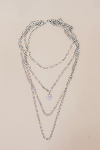 Layered silver chain necklace featuring multiple chain styles and a small pavé evil eye pendant. Trendy multi-chain jewelry for a bold, stacked look.