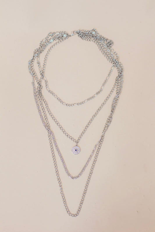 Layered silver chain necklace featuring multiple chain styles and a small pavé evil eye pendant. Trendy multi-chain jewelry for a bold, stacked look.