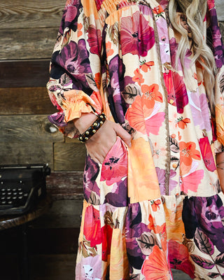 Women’s boho floral button front dress featuring a vibrant pink, purple and orange print, relaxed fit, long sleeves, ruffle details and side pockets.