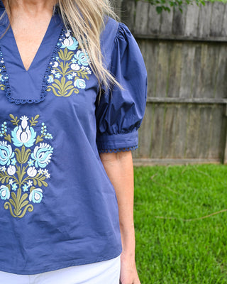 Navy blue embroidered blouse with puff sleeves, floral embroidery detail, and scalloped trim neckline, styled with white shorts for a chic summer boutique outfit.