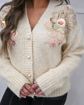 Beige cardigan with floral embellishments on a plain background