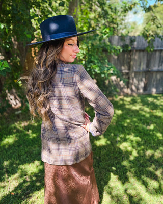 Back view of women's tailored plaid blazer in neutral brown, taupe and navy tones, styled with a brown satin midi skirt and black wide-brim western hat for a chic fall outfit.