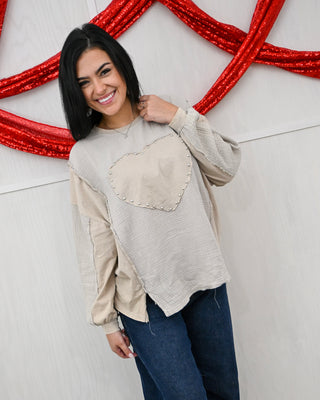 Woman wearing a beige sweater with a heart design against a decorative red and white background