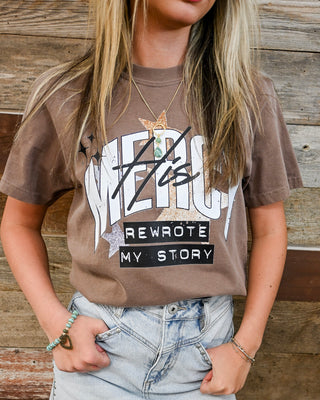 Women’s brown “Mercy Rewrote My Story” graphic t-shirt styled with light wash denim skirt, faith-based tee, casual boutique outfit, trendy everyday look.