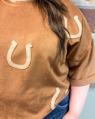 Brown suede top with embroidered horseshoe details, relaxed fit, and short sleeves styled with denim jeans