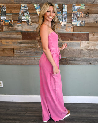 Women’s pink strapless wide leg jumpsuit with smocked waist, drawstring detail, and side pockets for a bold effortless boutique look