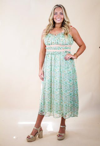 Woman wearing a green and cream floral two-piece set with ruffle-trim crop top and high-waisted midi skirt. Lightweight and breezy summer outfit perfect for vacations or garden parties.