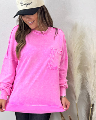 Woman wearing an oversized hot pink washed sweatshirt with a raw-edge front pocket, styled with dark jeans and a cream “Cowgirl” hat for a cozy casual look.
