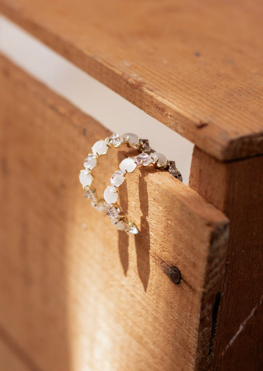 Pair of gold hoop earrings featuring alternating opal-inspired stones and faceted clear crystals, set in prong settings and displayed on a rustic wooden surface. Elegant and eye-catching statement hoops for special occasions.