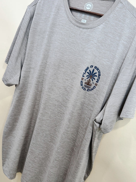 Men’s light gray performance t-shirt with small palm tree and Flag & Anthem logo detail on chest, displayed hanging in boutique. Breathable and casual fit.