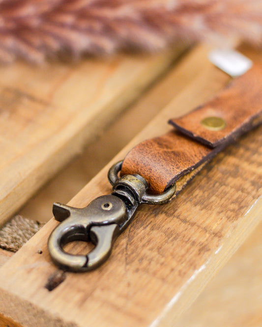 Close-up of a handmade brown leather keychain with brass hardware and swivel clasp on rustic wooden background