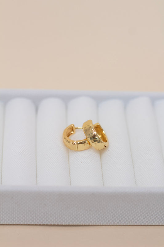 Pair of small gold hoop earrings with a hammered texture finish, displayed on a white fabric surface. Classic and stylish everyday hoops with a modern, artisanal look.
