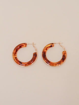 Pair of round hoop earrings with a glossy tortoiseshell pattern in warm brown and amber tones, finished with gold-tone hardware. Bold, retro-inspired statement earrings for everyday or dressy styling.