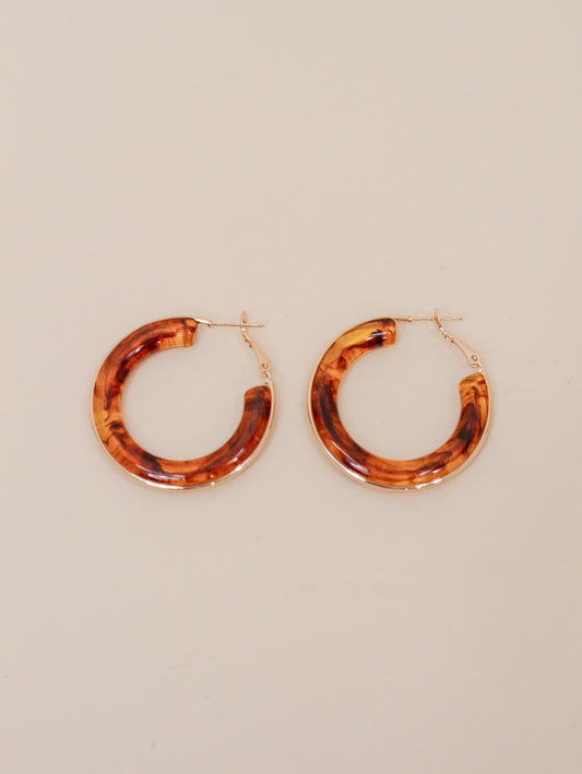 Pair of round hoop earrings with a glossy tortoiseshell pattern in warm brown and amber tones, finished with gold-tone hardware. Bold, retro-inspired statement earrings for everyday or dressy styling.