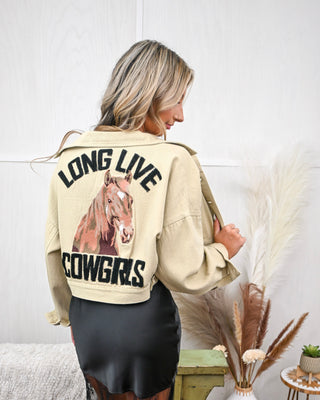 Back view of model wearing a cropped khaki jacket with bold "LONG LIVE COWGIRLS" lettering and horse graphic, styled over a black satin and lace midi dress.