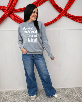 Woman wearing a gray sweatshirt with text and blue jeans standing against a decorative red and white wall.