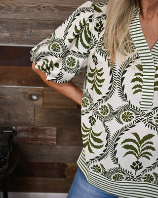 Ivory and olive green printed blouse with botanical pattern, striped V-neck trim and puff sleeves, styled with denim for an elevated casual look.