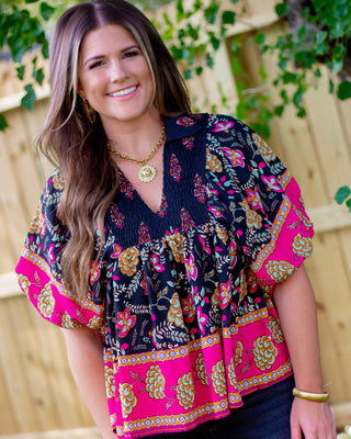 Woman wearing a navy floral blouse with pink and mustard boho patterns, featuring a smocked neckline and flutter sleeves for a chic fall boutique look.