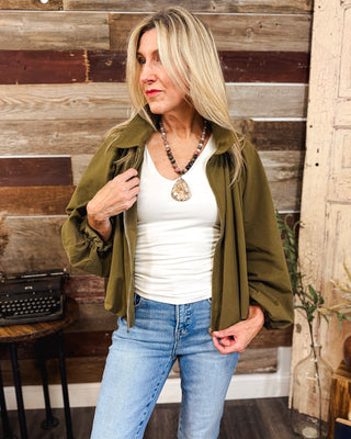 Women’s olive green balloon sleeve zip-up jacket styled with a white tank, light wash jeans and a statement stone pendant necklace for a chic fall look.