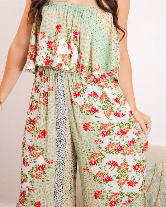 Close-up of a strapless floral patchwork jumpsuit with ruffle top detail and wide-leg fit, featuring red and orange blooms on soft green and cream fabric.