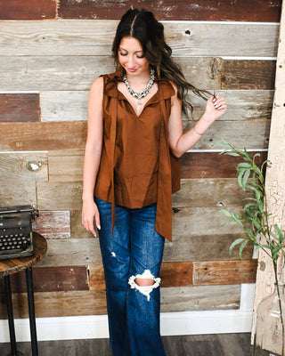 Women’s rust brown sleeveless ruffle blouse with tie-front detail styled with distressed wide-leg jeans for a chic, trendy fall boutique outfit.