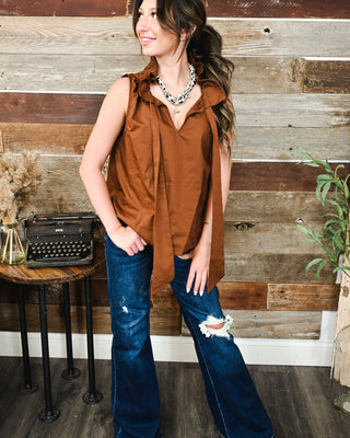Women’s rust brown sleeveless ruffle blouse with tie-front detail styled with distressed wide-leg jeans for a trendy fall boutique outfit.
