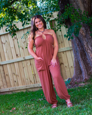 Woman wearing a strapless brown halter jumpsuit with pockets and gathered ankle hems, styled for a relaxed and chic outdoor look.
