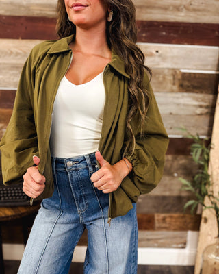 Women’s olive green zip-up jacket with dramatic balloon sleeves, collared neckline and relaxed fit, styled with a white tank and high-rise jeans.