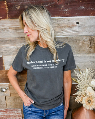 Women’s charcoal gray “Motherhood is my ministry” graphic t-shirt, faith-based Christian tee styled with denim jeans, casual everyday boutique outfit, soft relaxed fit top.