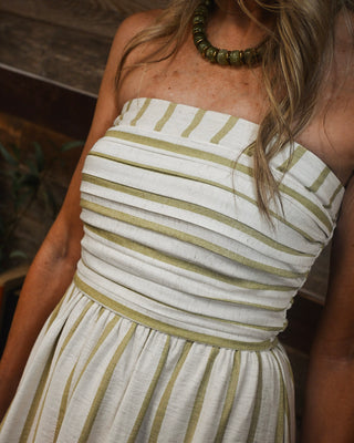 Women's strapless olive green and ivory striped midi dress with a smocked bodice and flowy skirt, styled with a chunky olive bead necklace for effortless summer boutique style.