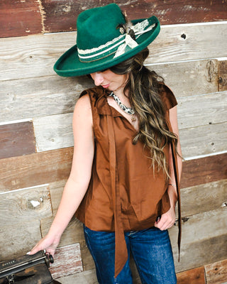 Model wearing a custom emerald green Western felt hat with lace ribbon, chain and feather details, styled with a brown sleeveless blouse and statement necklace.