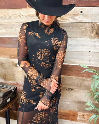 Women's black floral mesh maxi dress with rust-colored floral print, sheer long sleeves, and mock neckline, styled with a black western cowboy hat at MaKenzie Layne Boutique.