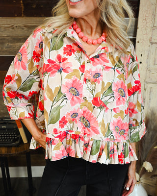 Women's cream floral button-front top with vibrant pink and coral flowers, olive green leaves, three-quarter sleeves and a feminine ruffle hem.
