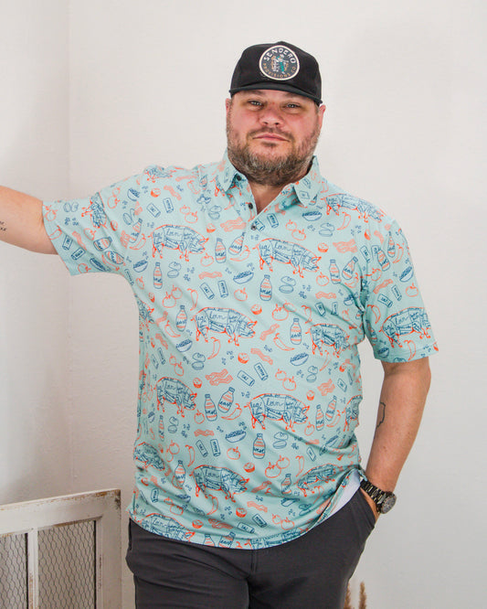 Man wearing a teal Sendero button-down shirt with BBQ illustrations and a black mesh Sendero Provisions Co. hat featuring a round embroidered patch.