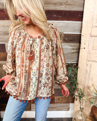 Women’s boho paisley floral blouse in cream, rust and earthy tones with tassel tie neckline, balloon sleeves and pom-pom trim for an effortless fall look.