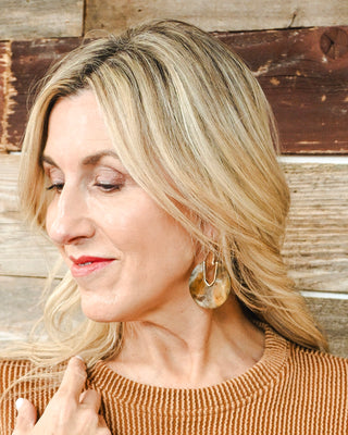 Oversized marbled statement earrings in amber, ivory and brown with gold-tone geometric accents, styled with a warm rust knit top for a chic fall look.