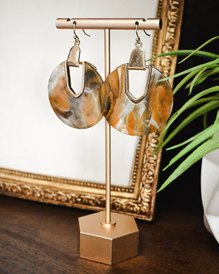 Oversized marbled statement earrings in warm amber, ivory and brown tones with gold-tone geometric accents and fishhook closures.