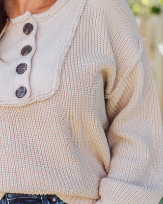 Close-up of a cream knit sweater featuring large tortoiseshell buttons and textured ribbed detailing, styled casually with denim for a cozy fall outfit.