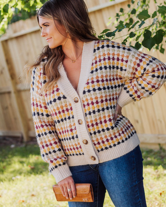 Close-up of woman wearing a cozy multicolor checkered knit cardigan with button front, paired with blue jeans and a tan wallet for a stylish fall outfit.