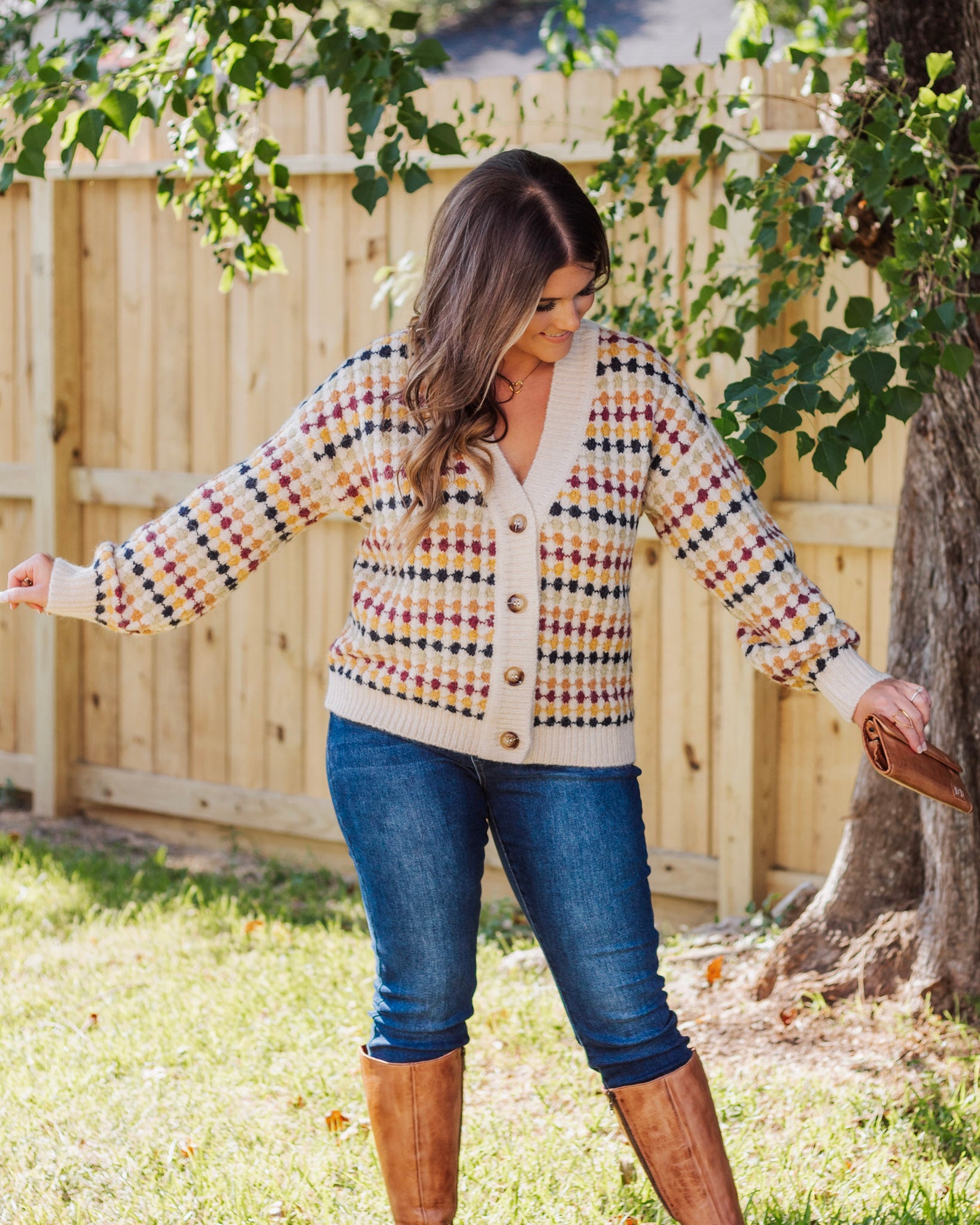 Woman wearing a cozy button-front cardigan with multicolor checkered pattern, paired with dark skinny jeans and tan knee-high boots for a fall-ready look.