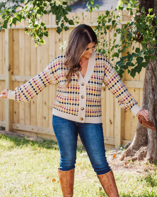 Woman wearing a cozy button-front cardigan with multicolor checkered pattern, paired with dark skinny jeans and tan knee-high boots for a fall-ready look.