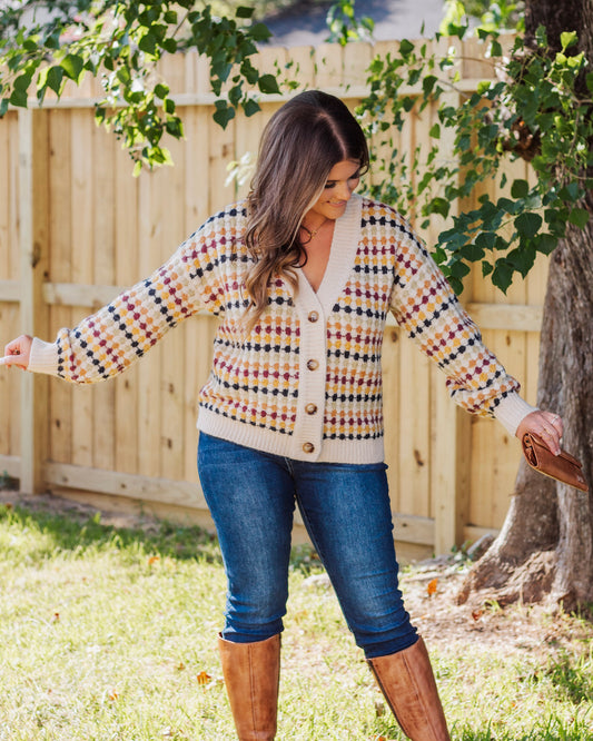 Woman wearing a cozy button-front cardigan with multicolor checkered pattern, paired with dark skinny jeans and tan knee-high boots for a fall-ready look.